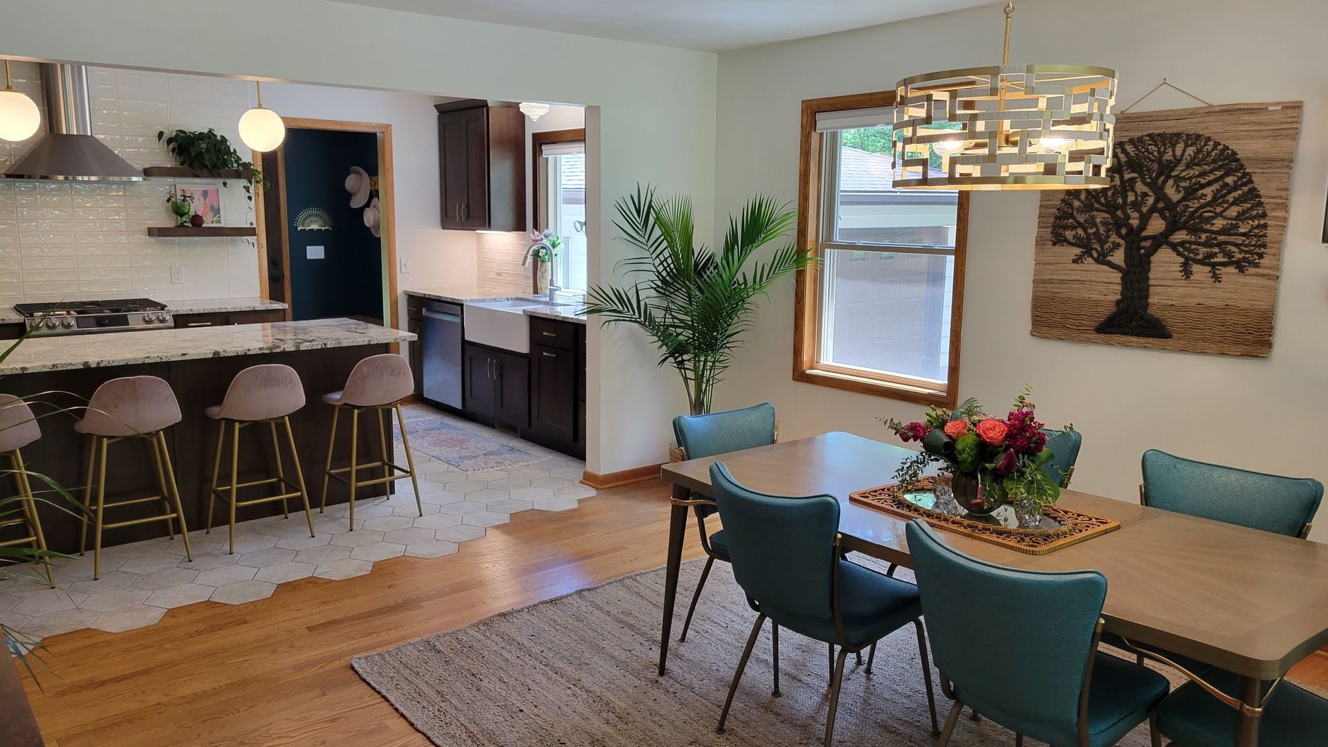 Open-concept dining and kitchen with teal chairs, a wood table, a kitchen island with barstools, and a decorative light fixture.
