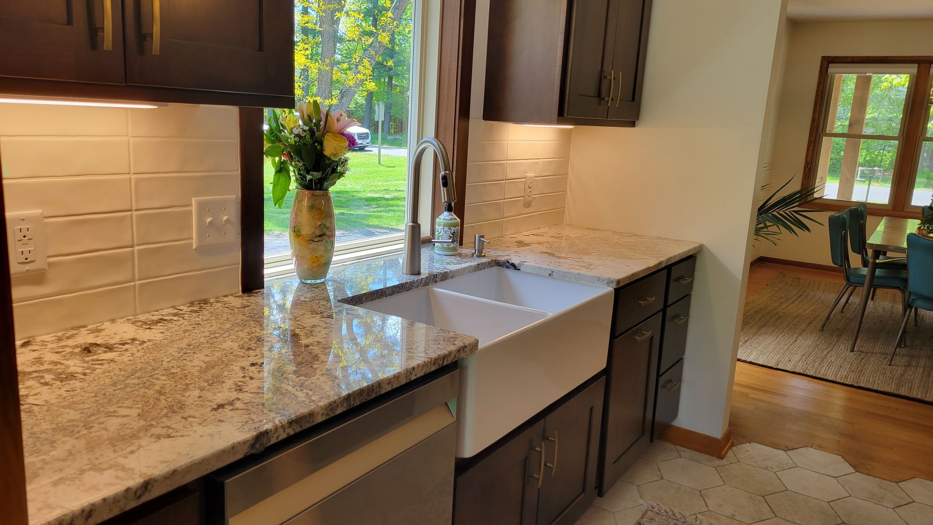 Kitchen with dark cabinets, white farmhouse sink, granite countertops, and a window overlooking greenery.