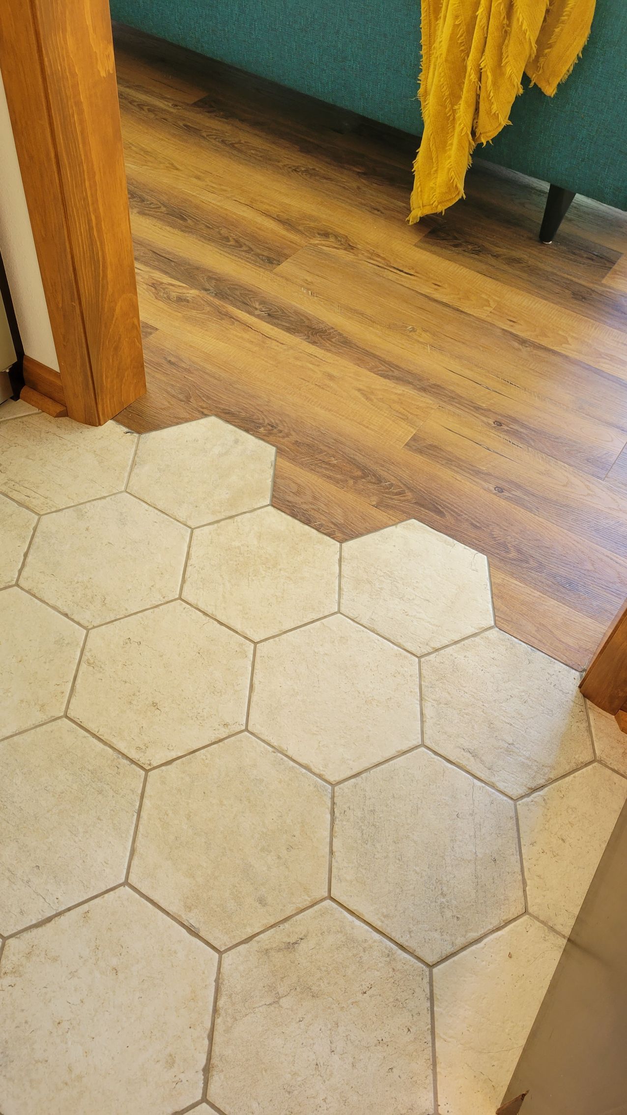Hexagon tile floor meets wooden floor, doorway with yellow fabric in background.