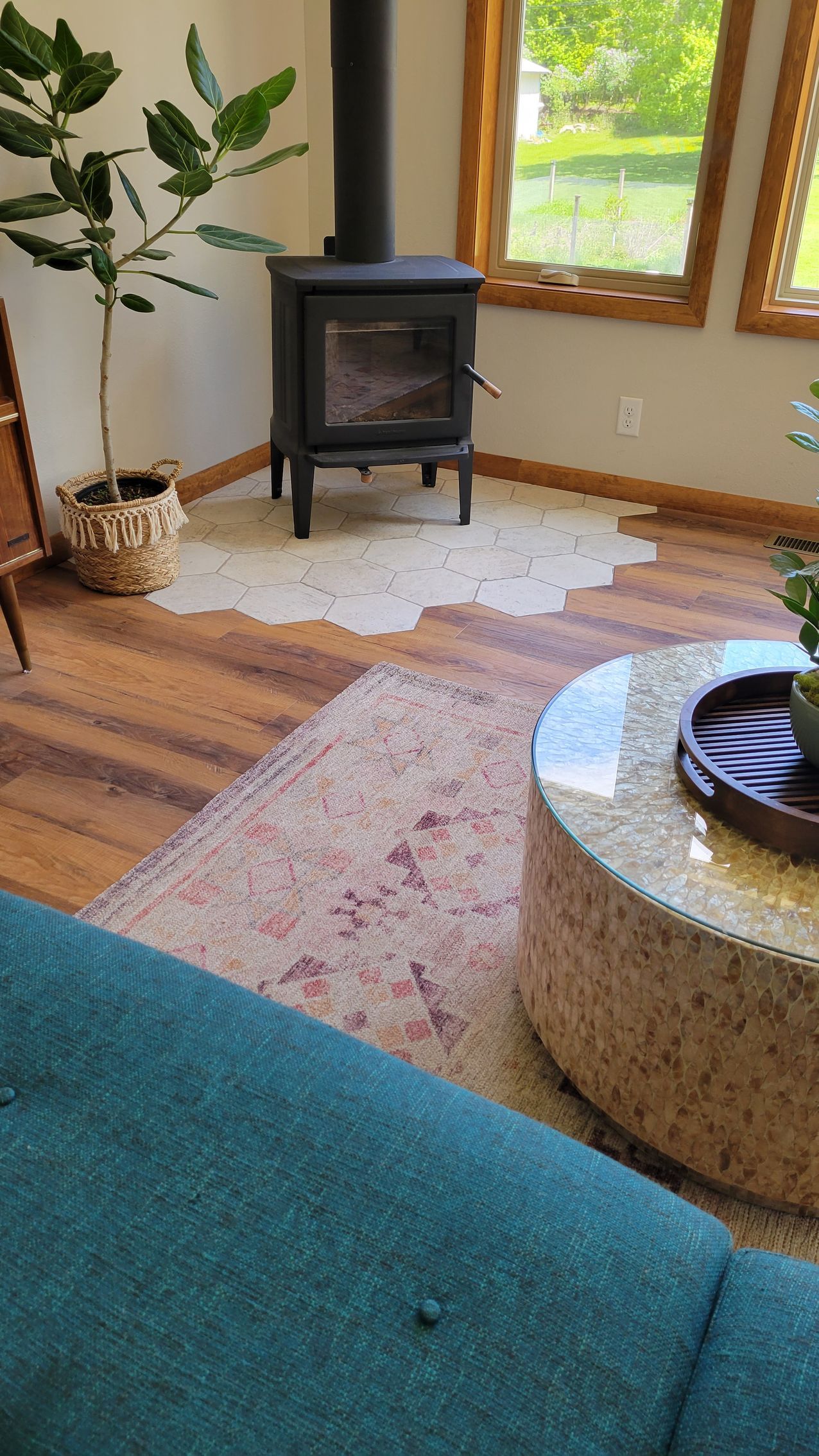 Living room with wood stove, area rug, coffee table, and teal sofa.