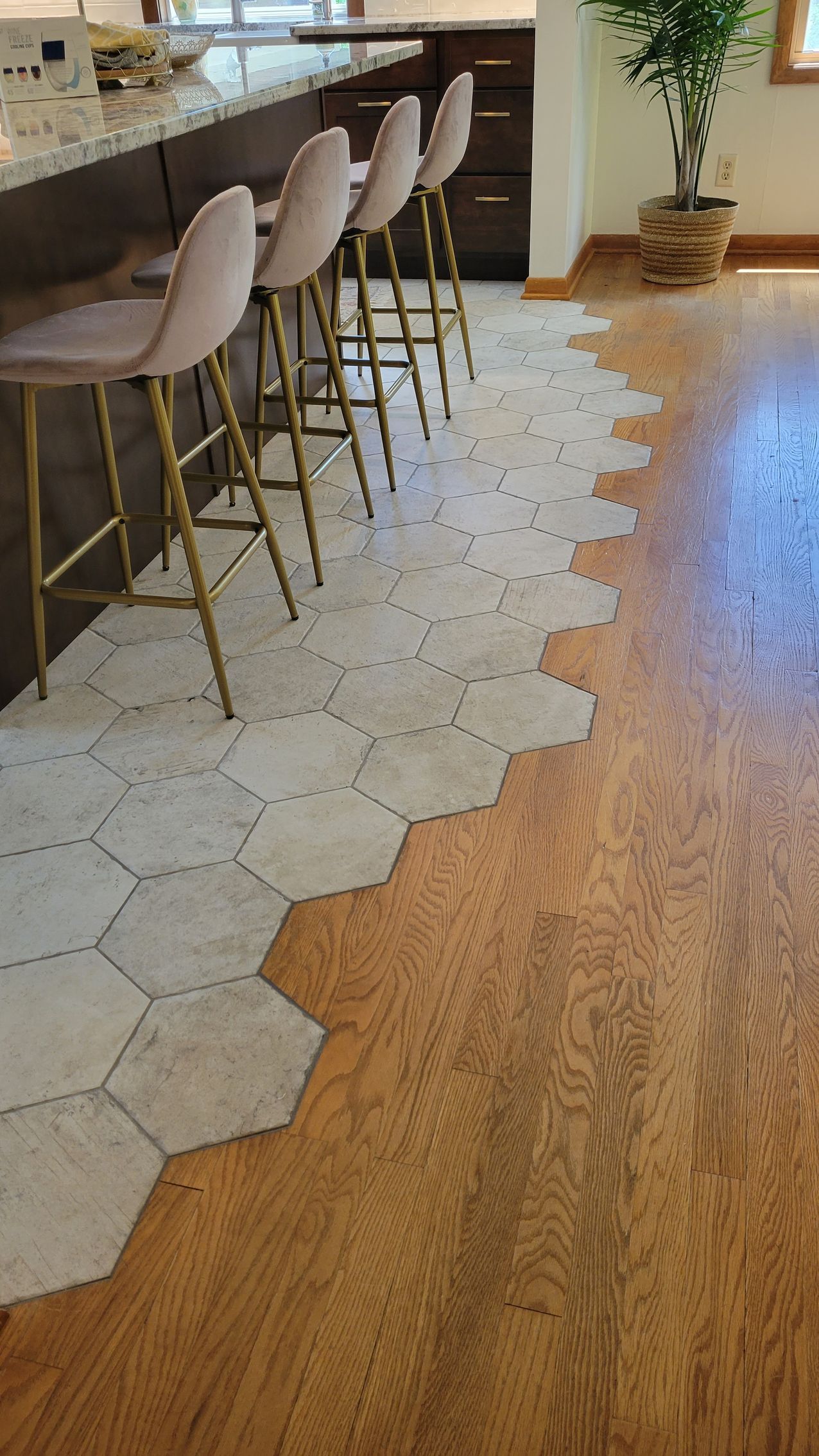 Hexagon tile floor transitions to wood floor, with bar stools at a counter in a kitchen.
