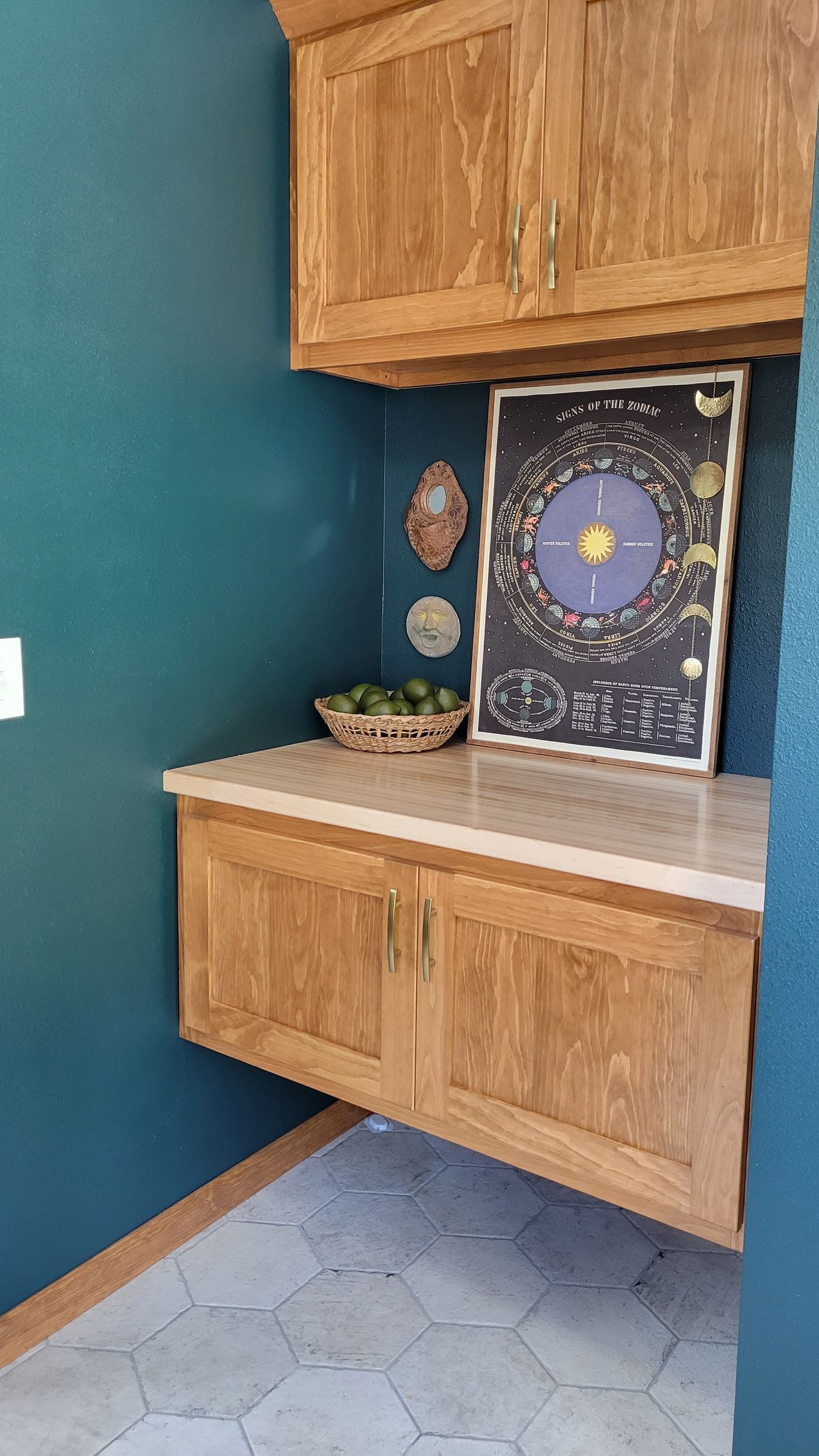 Built-in cabinetry in a pantry. Teal walls, wood cabinets, stone countertop, a cosmic art piece, and a basket of limes.