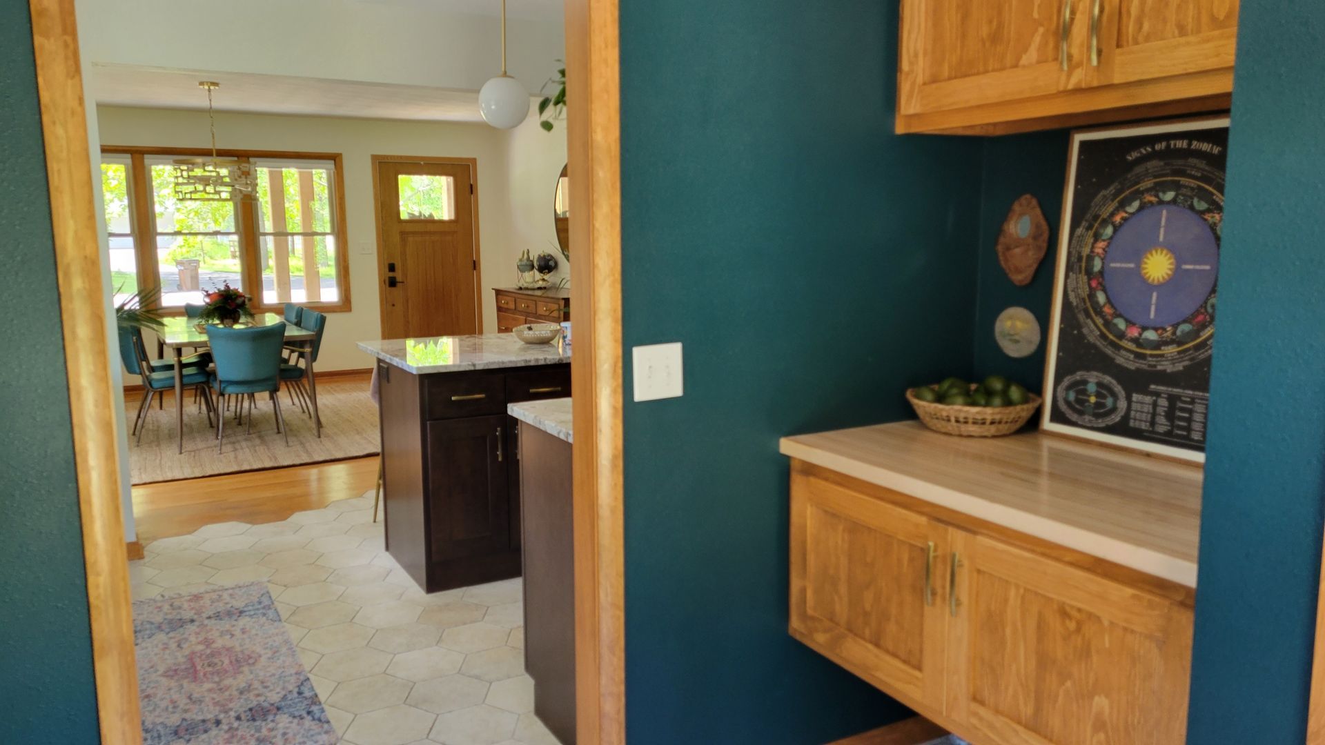 View from doorway into kitchen, dining area visible. Dark blue walls, light cabinets, island.