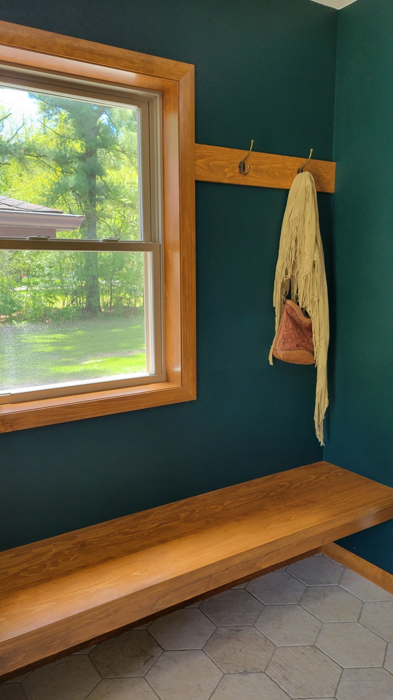 Teal-painted room with wooden bench, window, and coat rack with items hanging.