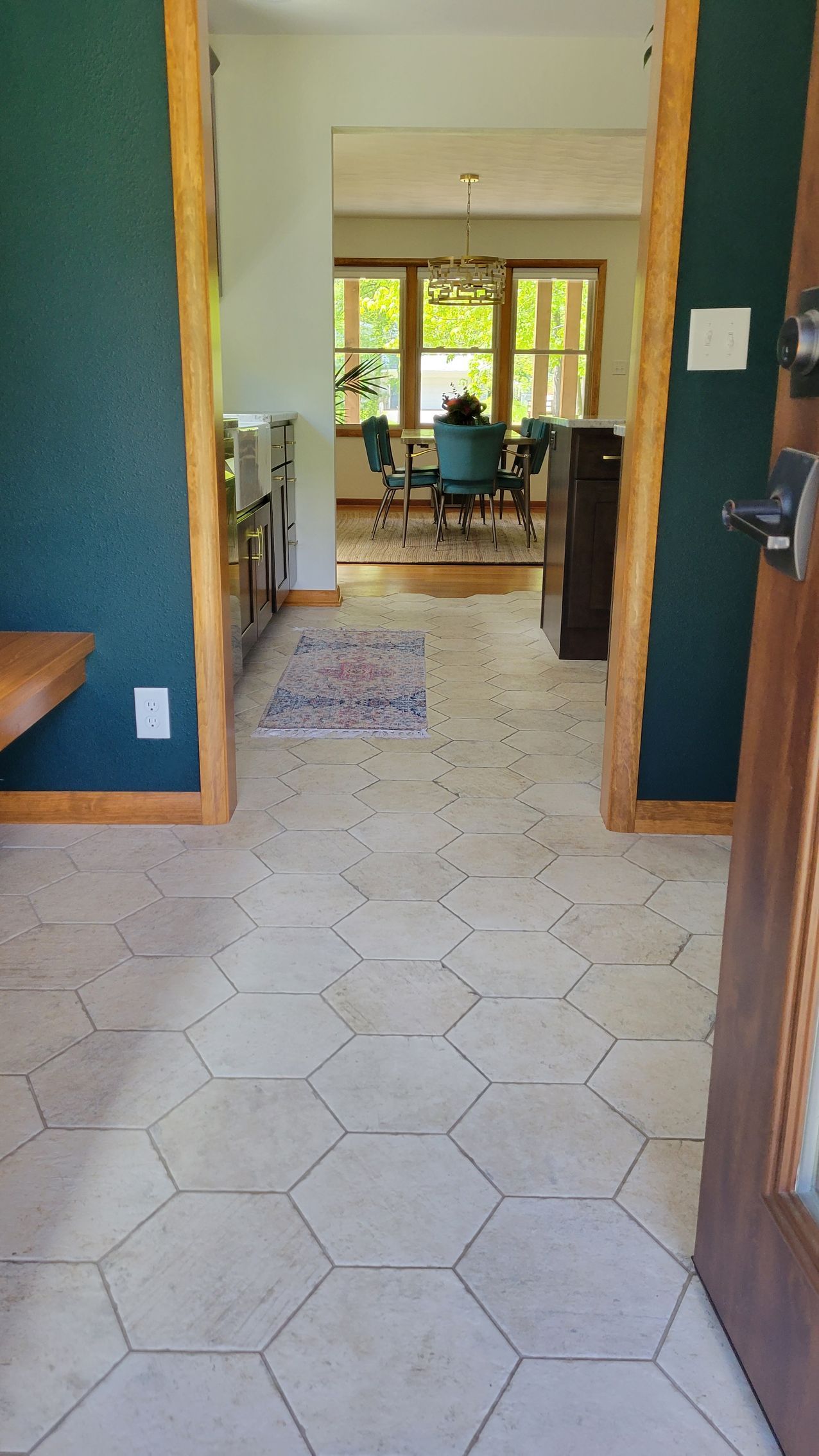 View from a doorway into a home. Hexagon tile floor leads to dining room with table and chairs. Teal walls.