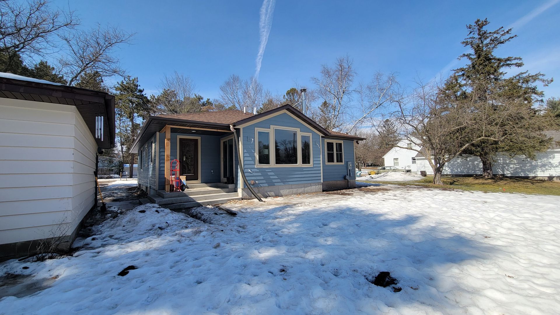 Blue house with snow on the ground, trees in the background, clear blue sky.