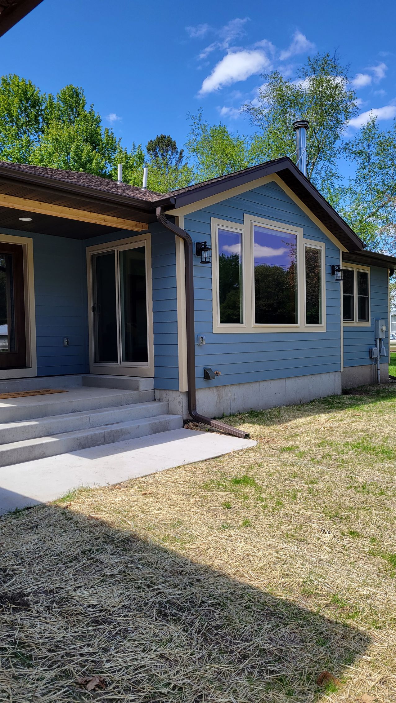 Blue house with brown trim and windows, light gray steps, and green grass.