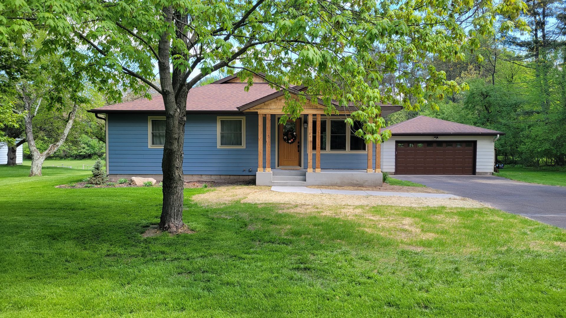 Blue house with brown roof and attached garage, in a green lawn setting.