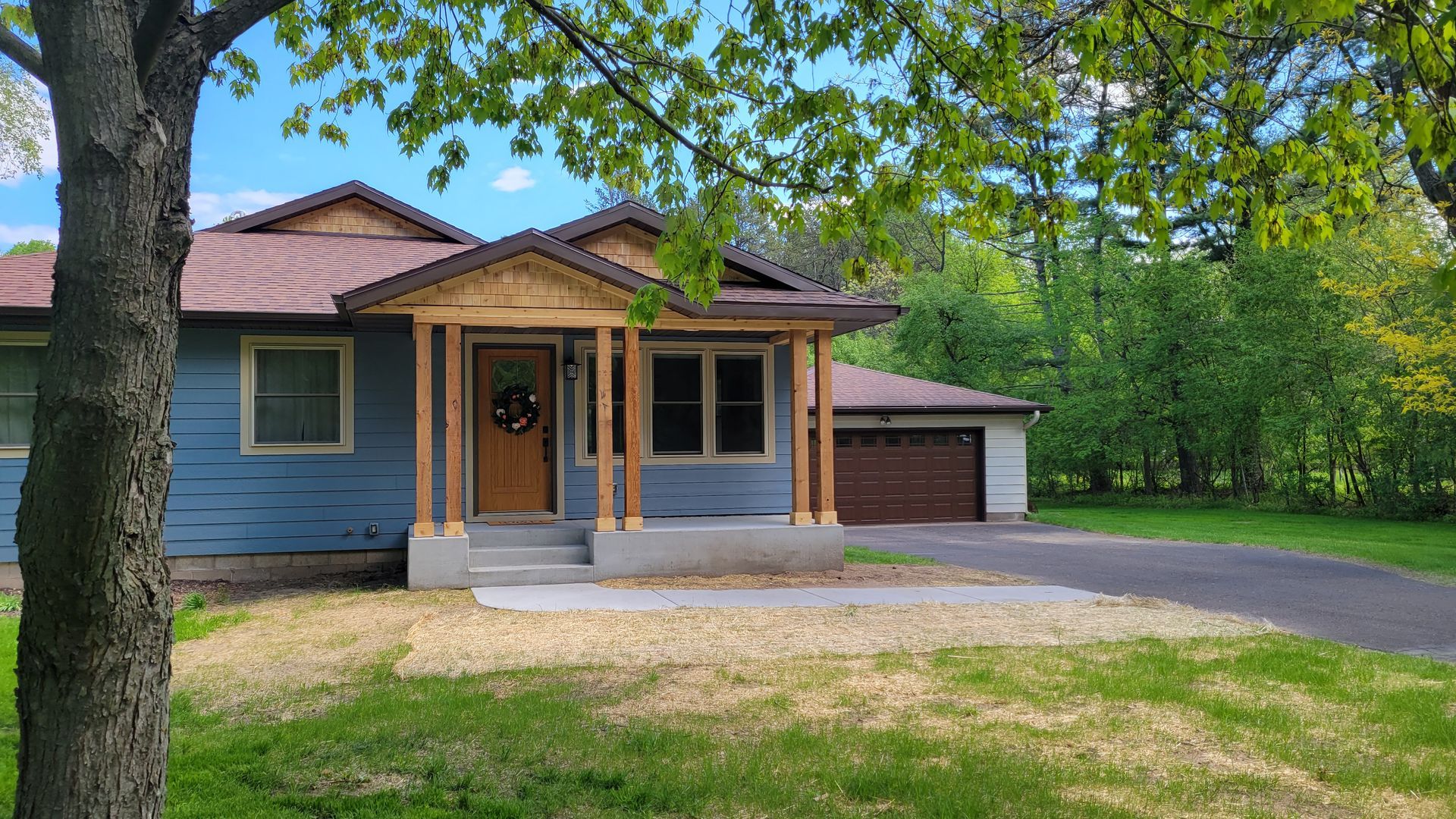 Blue house with brown trim and door, a small porch, and a driveway.