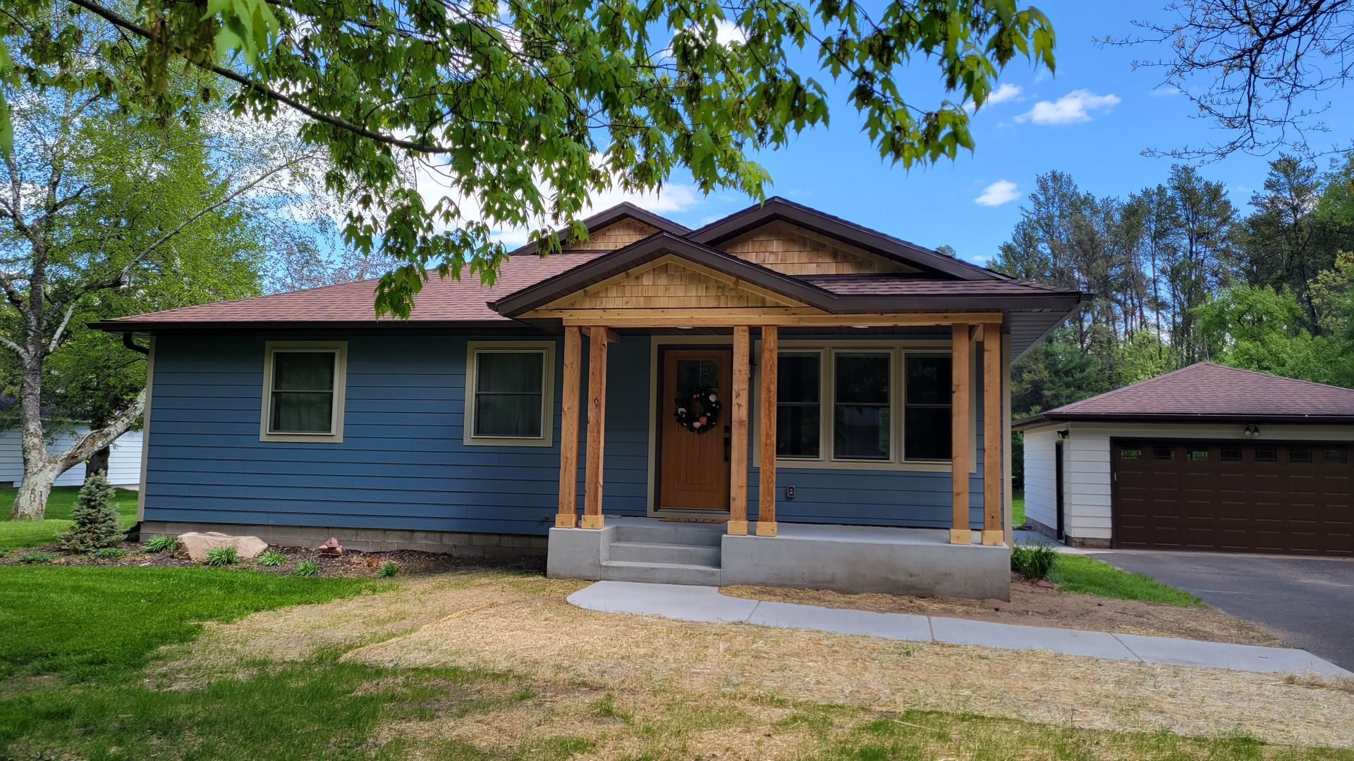 Blue house with brown trim and roof, small porch with steps, driveway and garage in background.