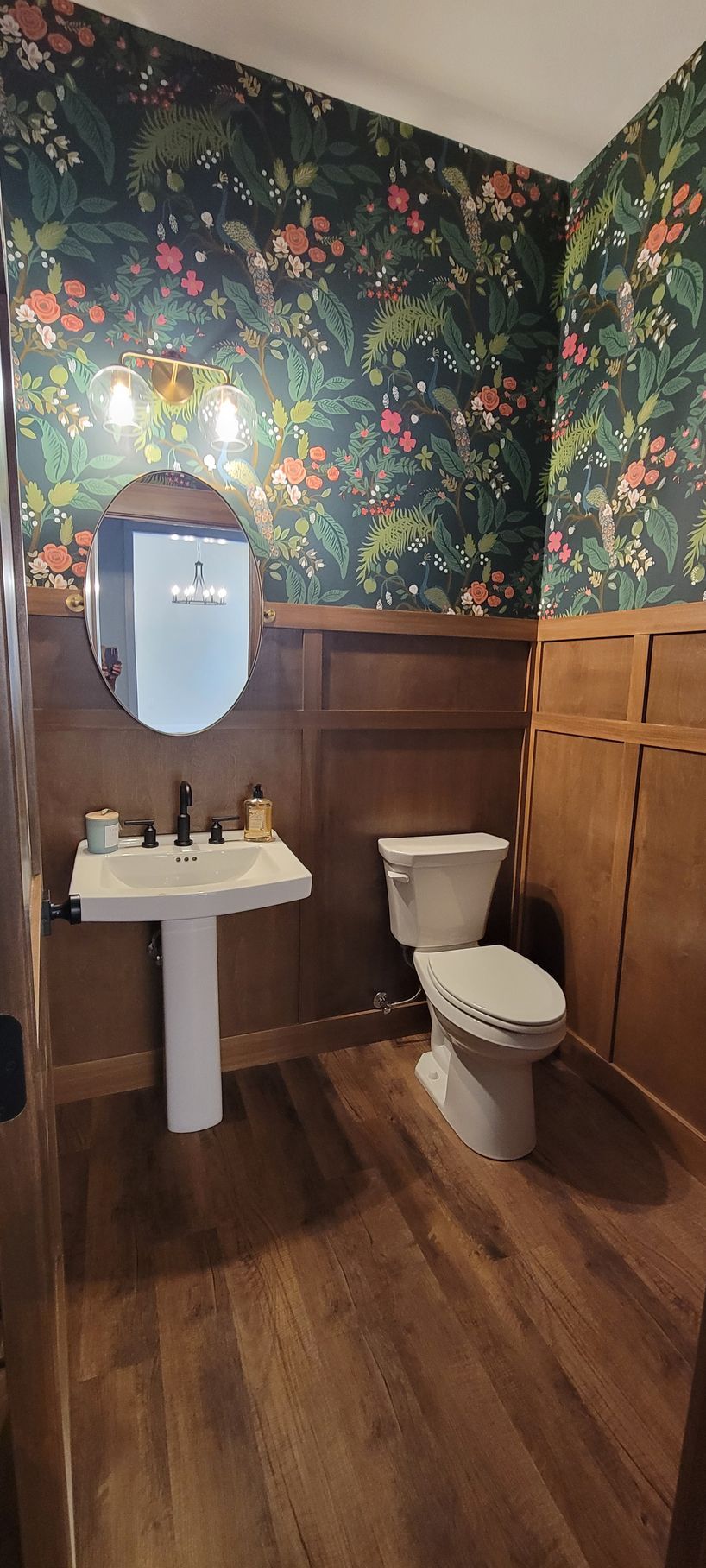 Small bathroom with dark floral wallpaper, wood paneling, and a pedestal sink.