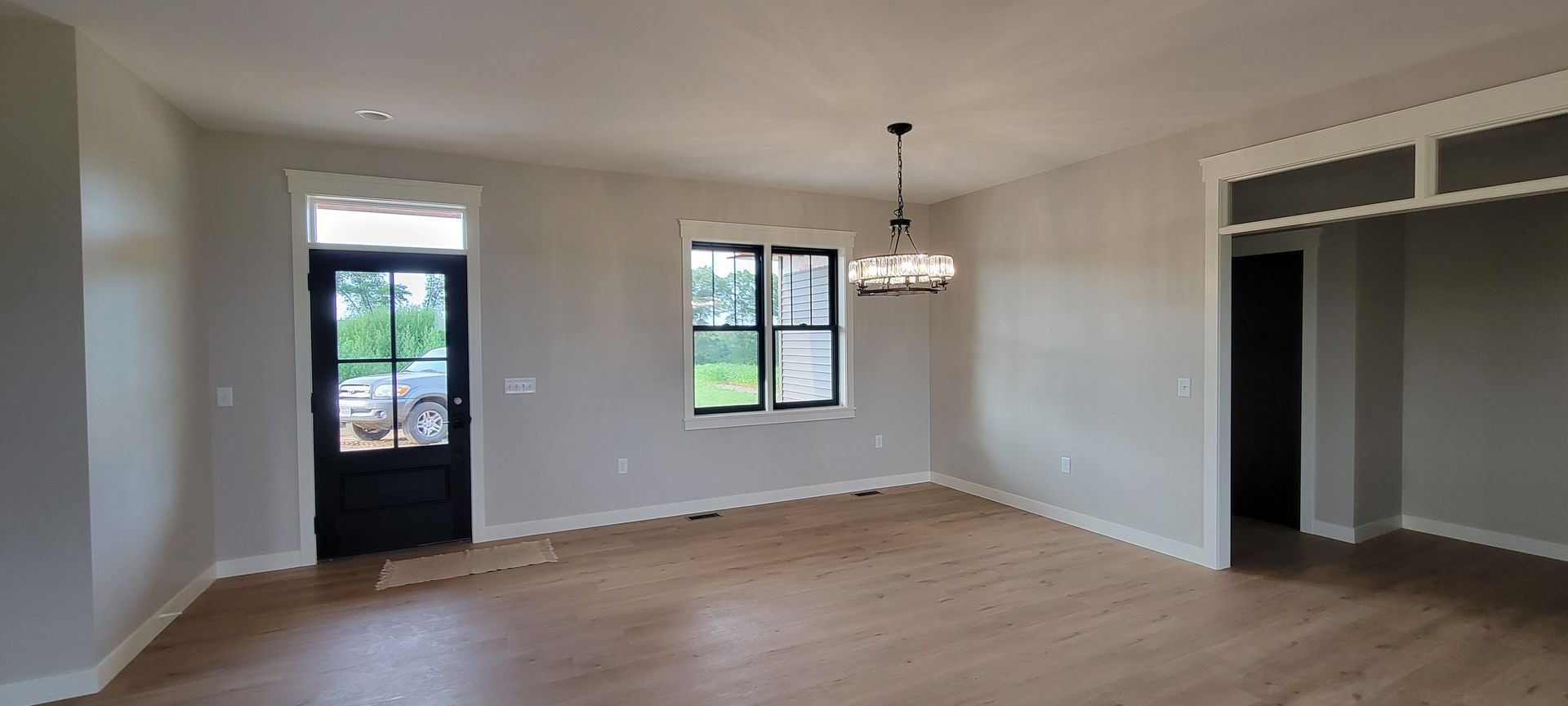 Interior of a room with a black front door, window, chandelier, and hardwood floors.