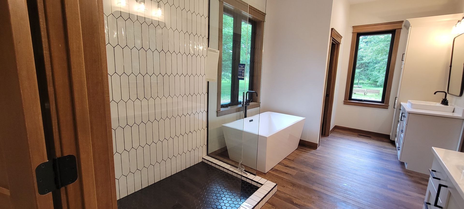 Bathroom with shower, tub, vanity, and windows, wood floors and trim, white walls, and bright natural light.