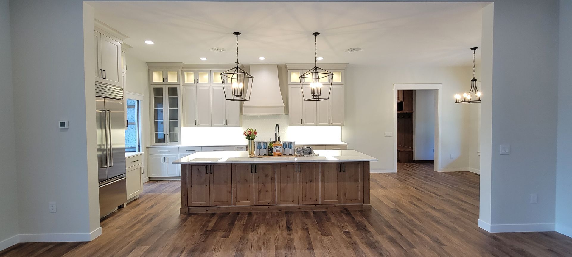 A modern kitchen with a large island made of wood and white countertops, wooden floor, and white cabinets.
