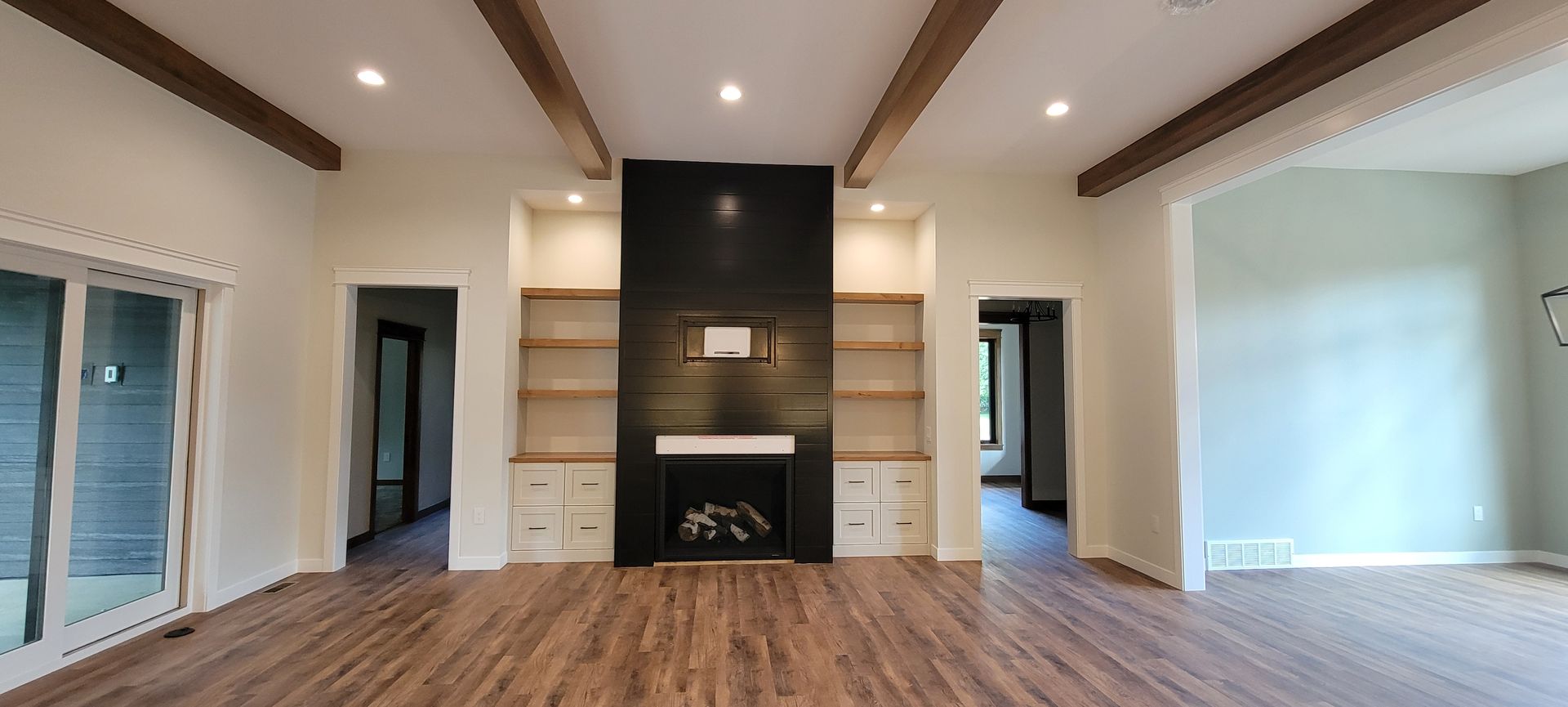 Living room with fireplace, built-in shelving, wooden beams, and hardwood floors.