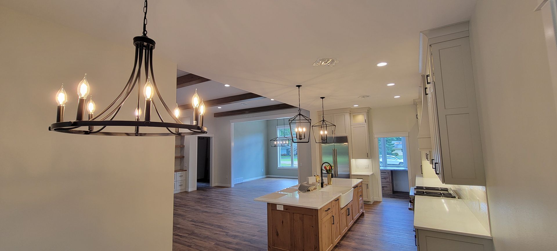 Open-concept kitchen with chandelier, island, and wood flooring. Light gray cabinets and white countertops.