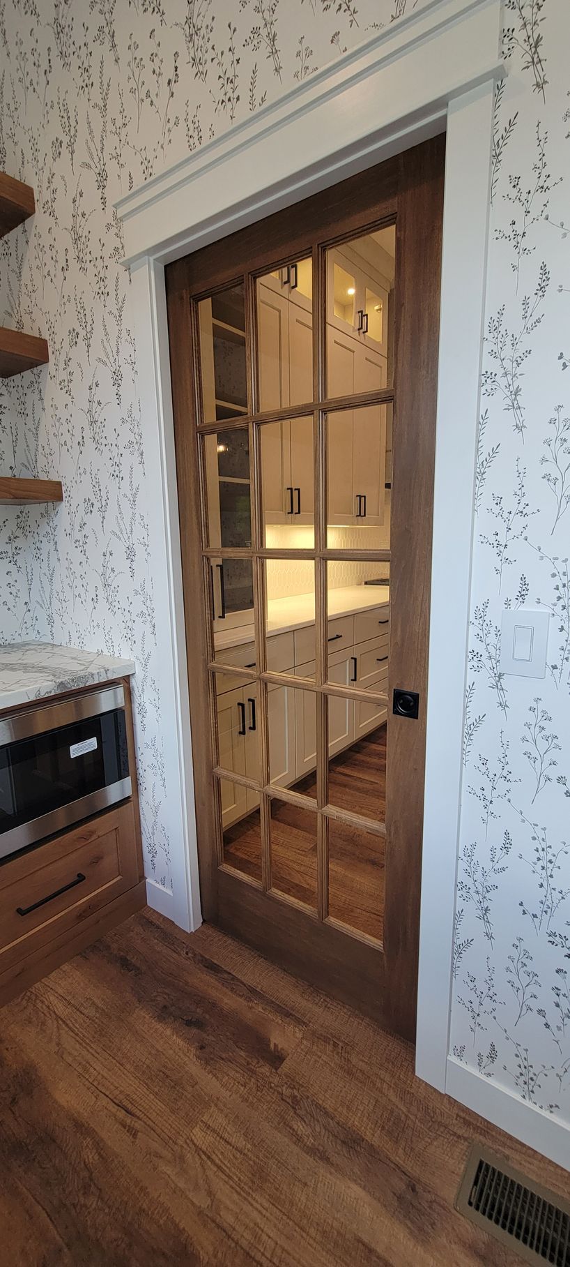 Wooden door with glass panes leading to a kitchen with white cabinets.