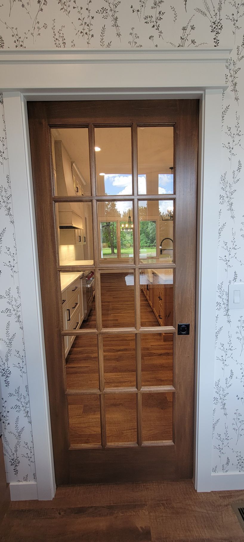 A wooden door with glass panels leads to a room with hardwood floors. The door has a black handle.