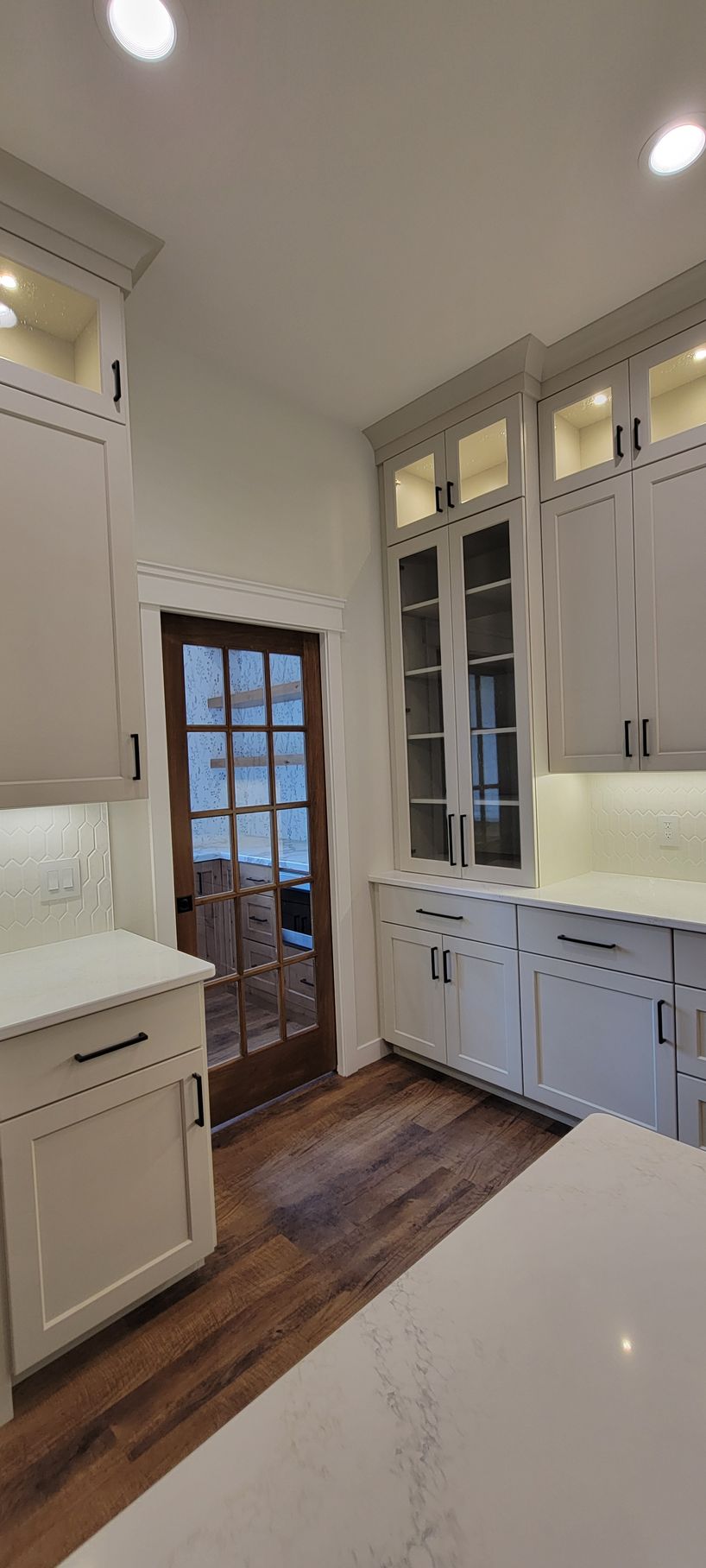 Kitchen with white cabinets, dark wood door, and hardwood floor.