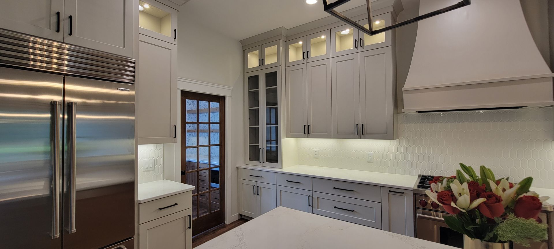A bright, modern kitchen with white cabinetry, stainless steel appliances, and a flower arrangement on the countertop.