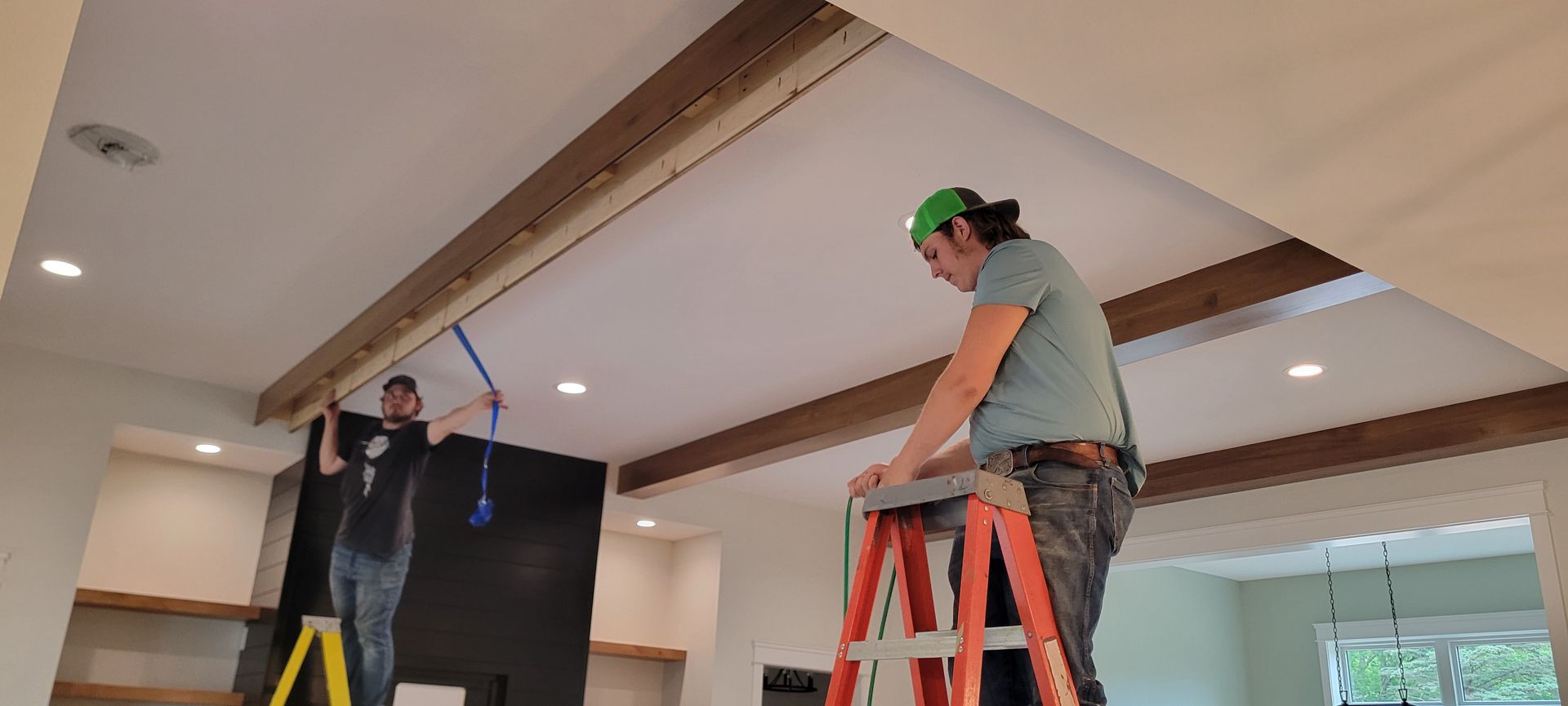 Two people installing wooden beams on a ceiling. One on a ladder, the other on a step ladder.