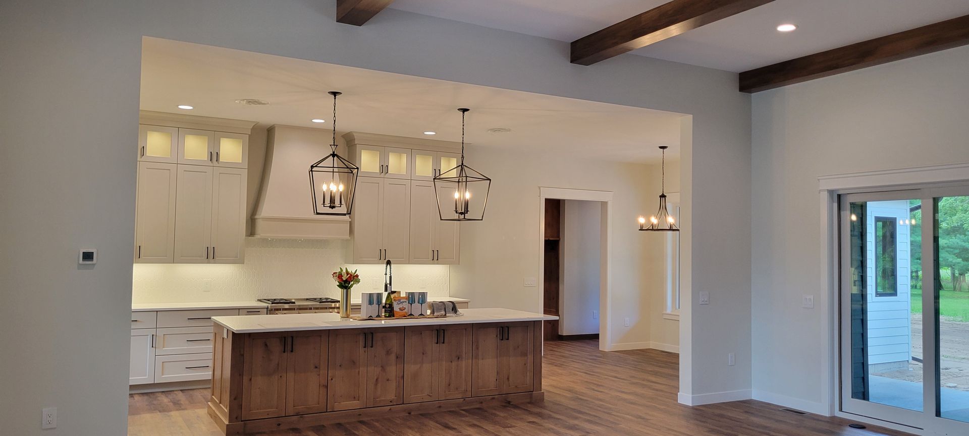 Kitchen interior with island, white cabinets, wood beams, and pendant lights.