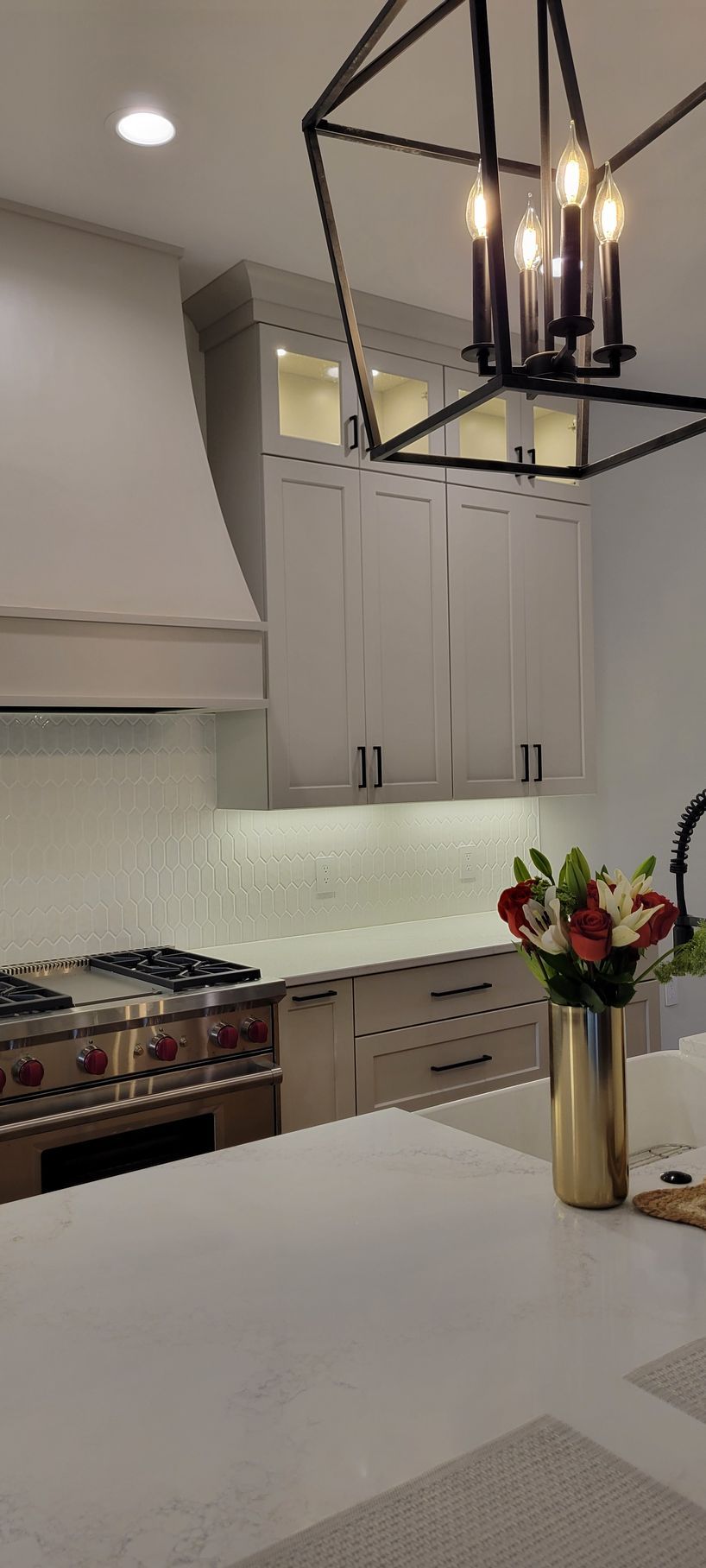 Modern kitchen with light cabinets, stainless steel appliances, and a black chandelier.