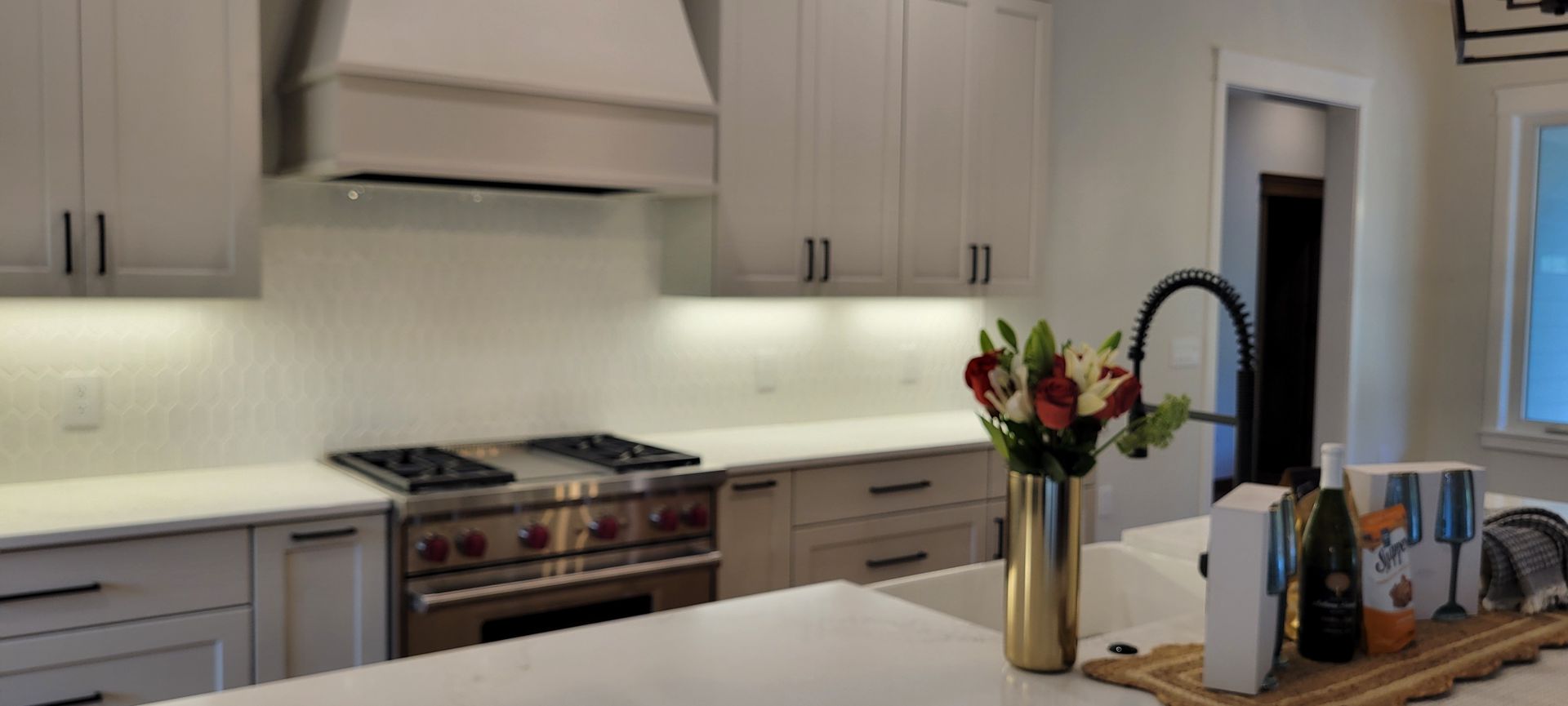 Kitchen interior with light cabinets, range hood, and island with flowers.