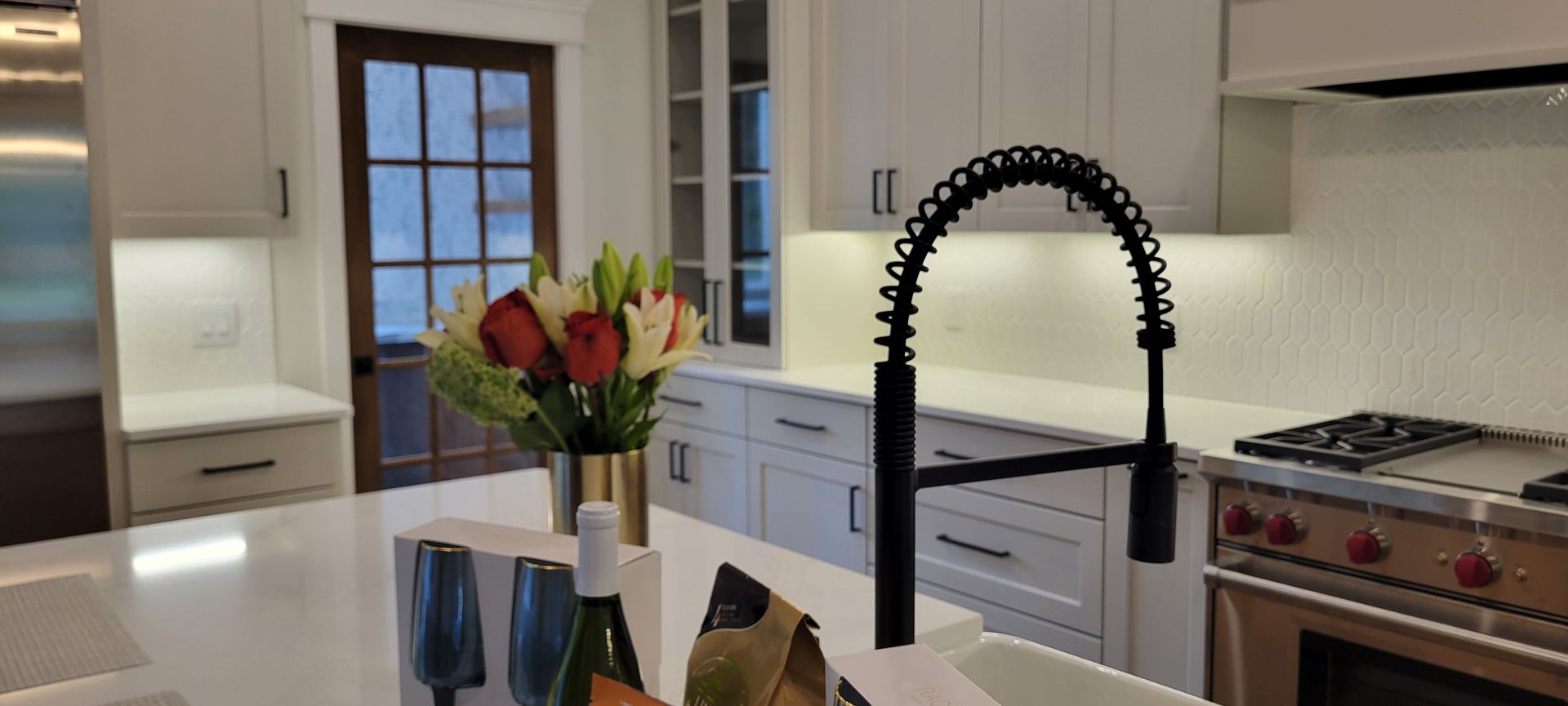 Kitchen with white cabinets, stainless steel appliances, and a black faucet. A bouquet sits on the island.