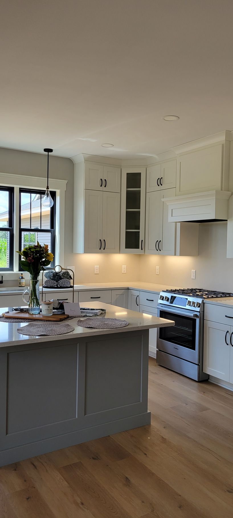 A kitchen with white cabinets, a gray island, stainless steel stove, and wood floors.