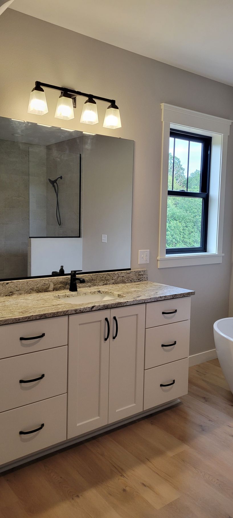 Bathroom with white vanity, black hardware, granite countertop, mirror, window, and wood floor.