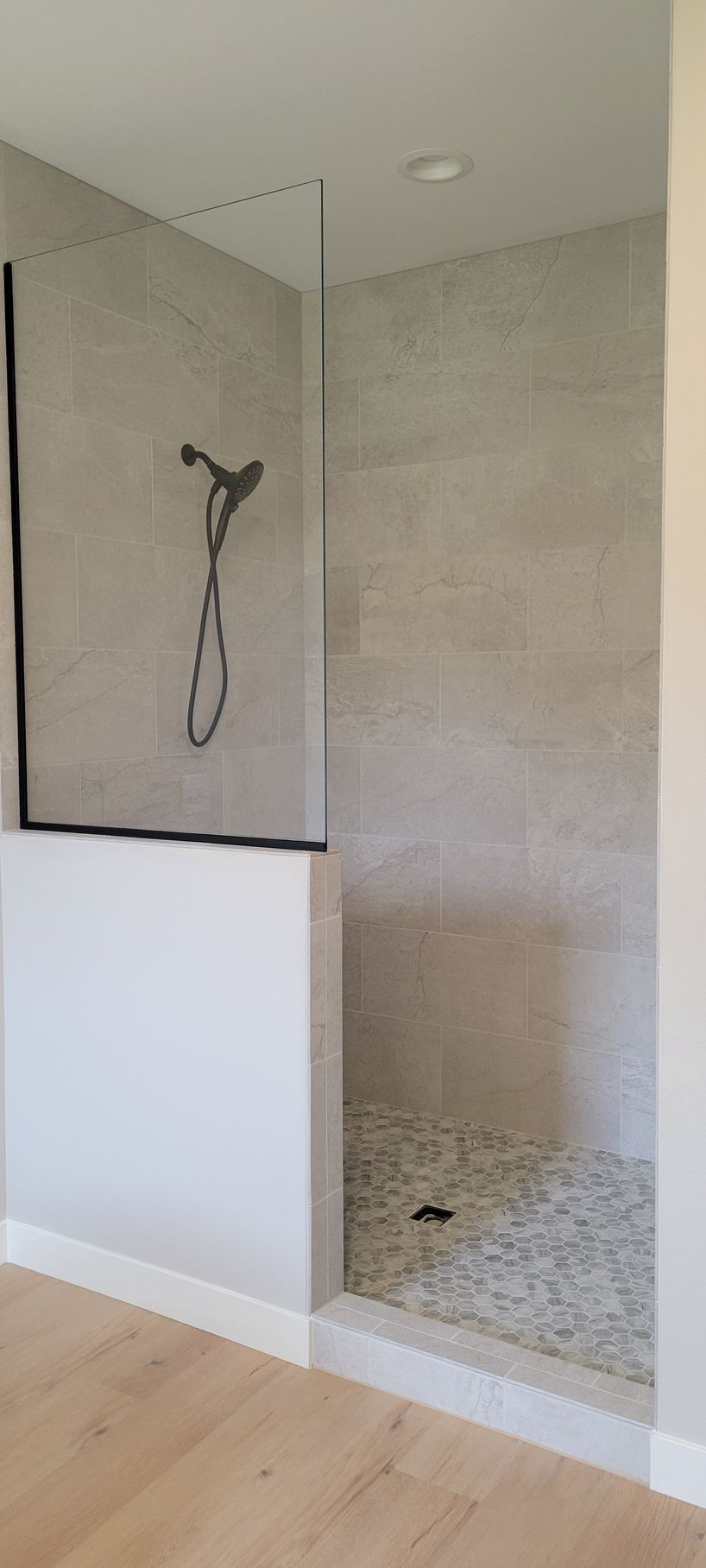 A modern shower with a glass door, pebble floor, and gray tiled walls.