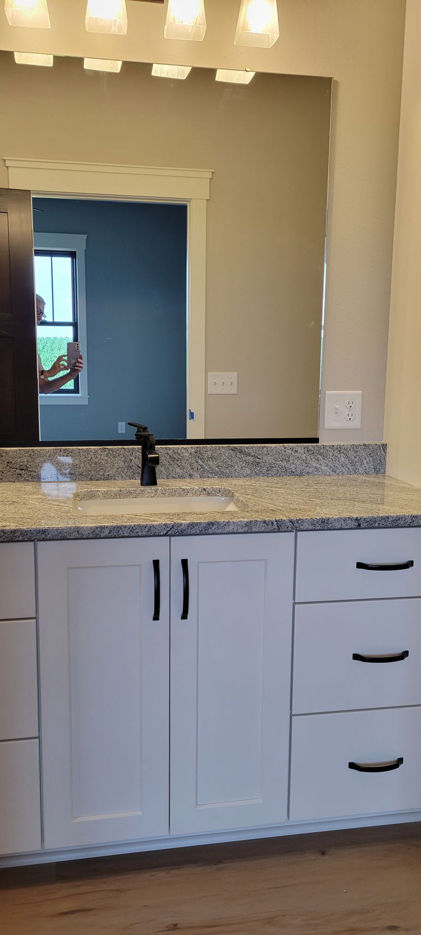 Bathroom vanity with white cabinets, granite countertop, black faucet, and large mirror.