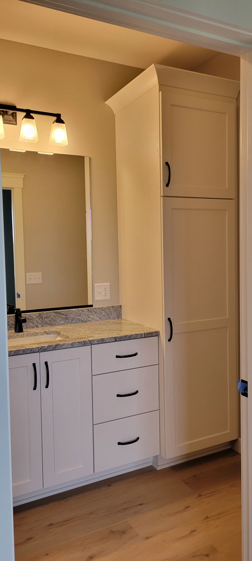 Bathroom vanity with a tall cabinet and dark hardware. Light wood flooring.