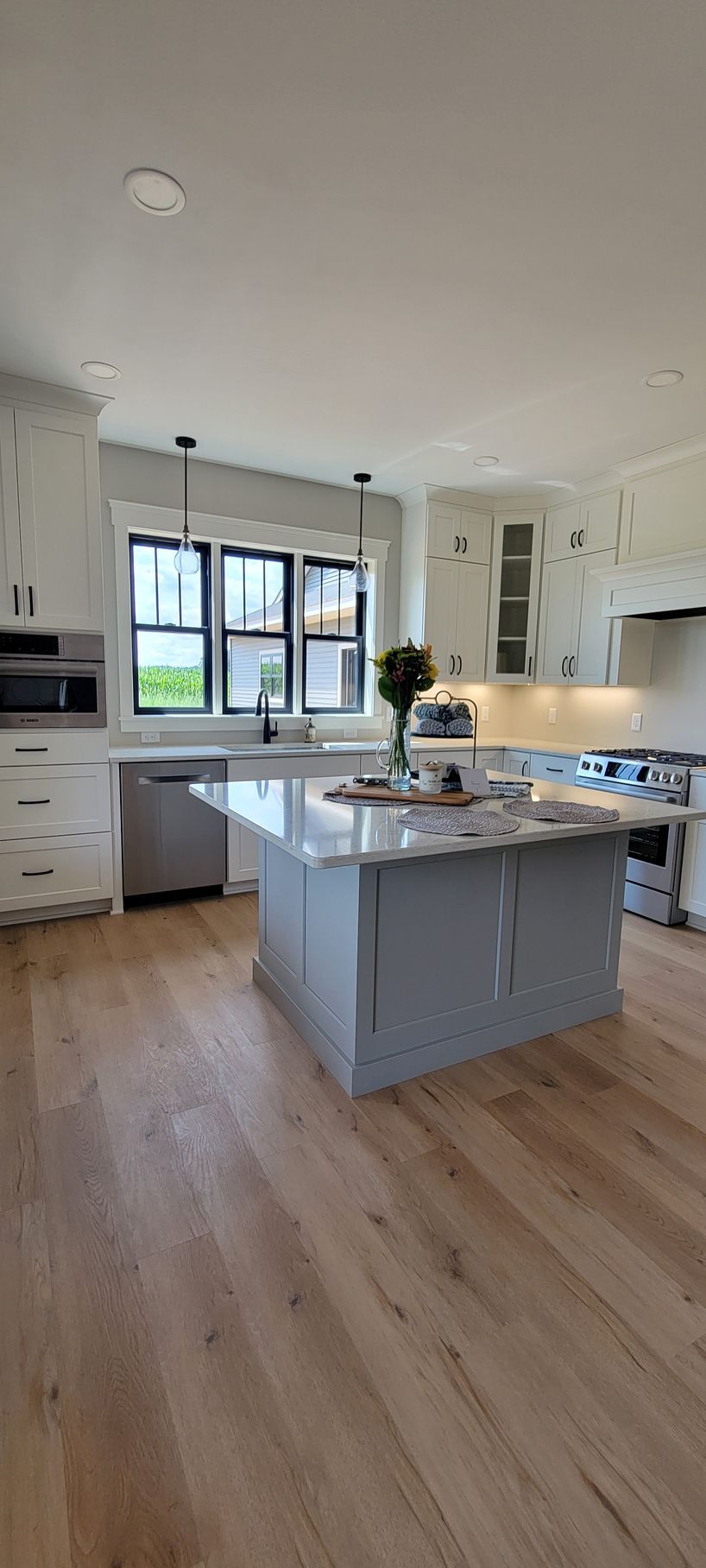 Kitchen with light wood floors, a gray island, white cabinets, and a window.