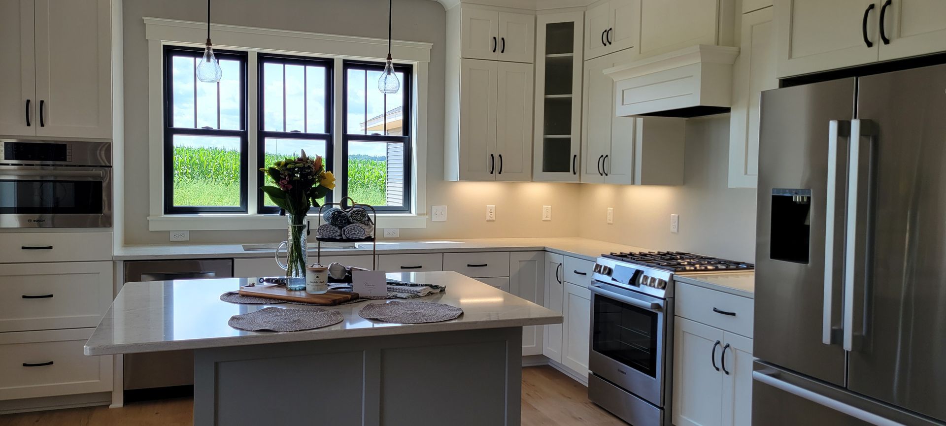 Modern white kitchen with a stainless steel refrigerator, island, and window.