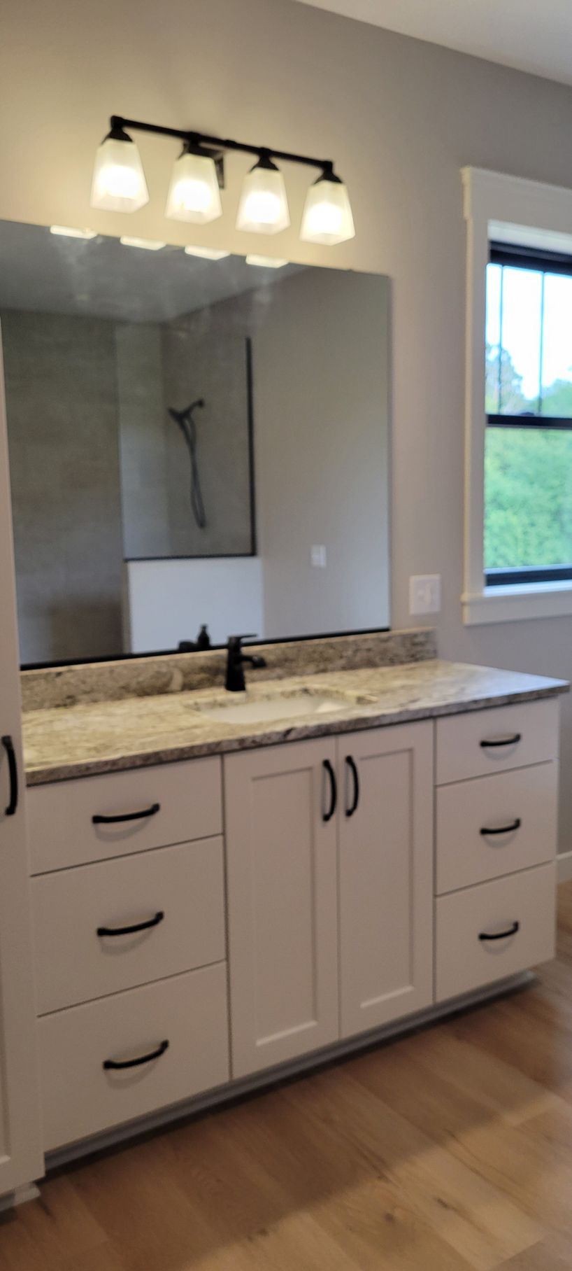 Bathroom vanity with white cabinets, black hardware, granite countertop, mirror, and light fixture.