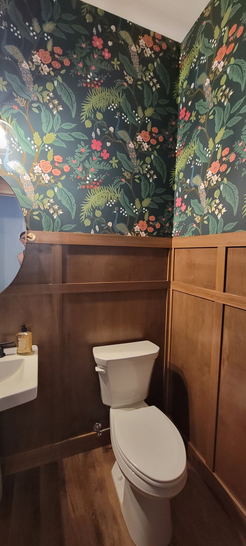 Small bathroom with floral wallpaper, wooden paneling, white toilet, and sink.
