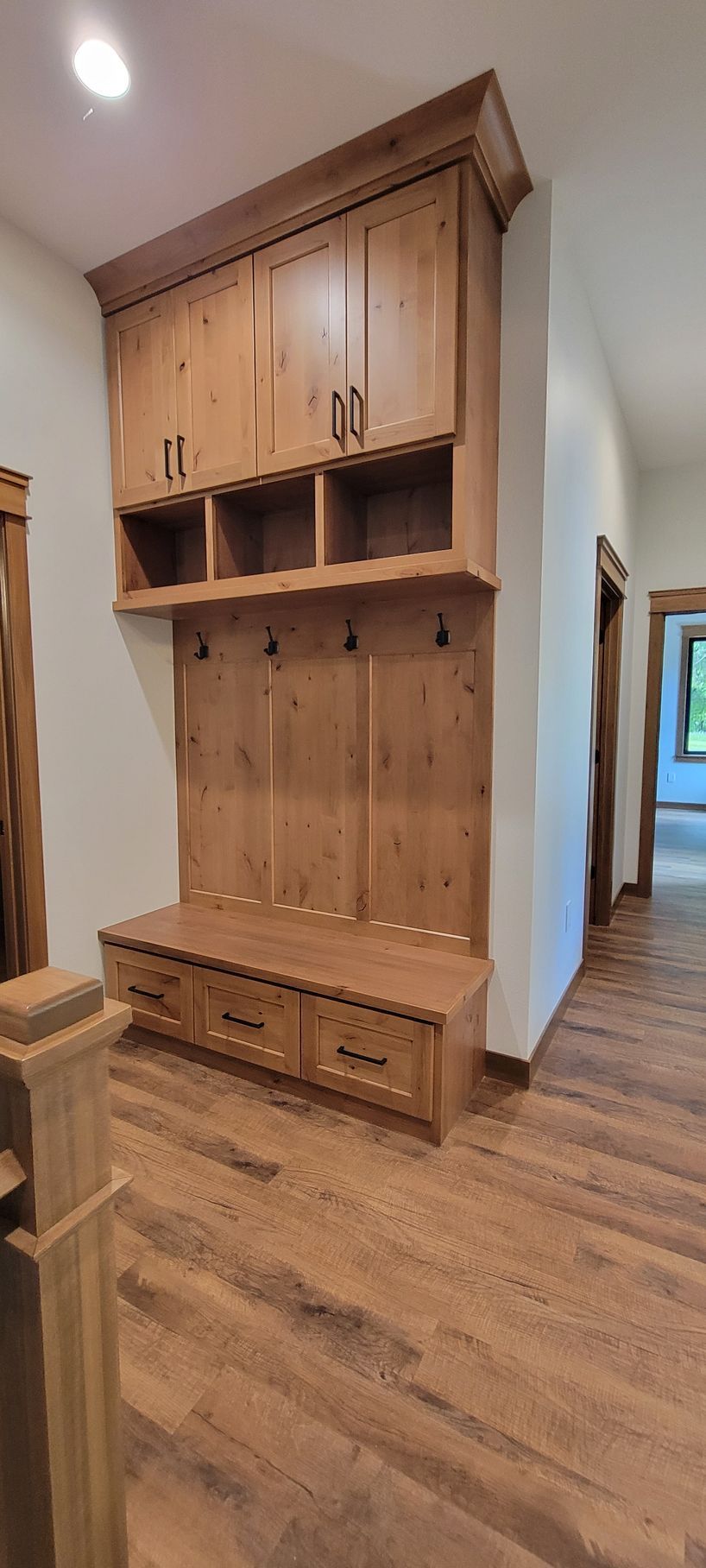 Wooden built-in entryway bench with cabinets, drawers, and hooks, in a home with wooden flooring.