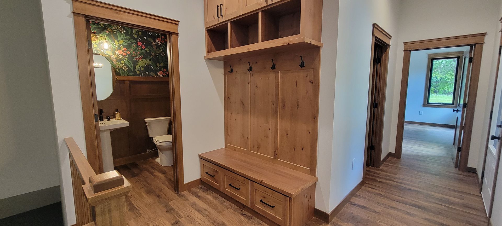 Hallway with wooden trim, built-in storage bench, and an open doorway to a bathroom with floral wallpaper.