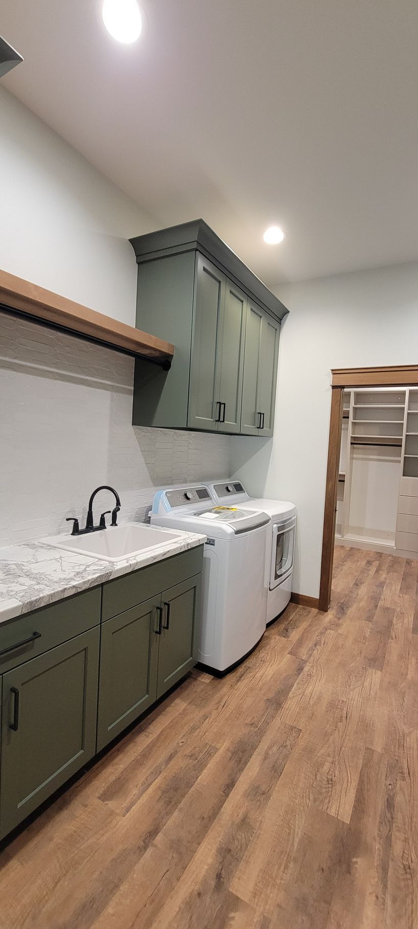 Laundry room with sage green cabinets, white countertops, and wood-look flooring. Washer and dryer are present.