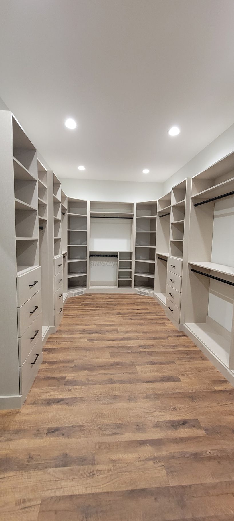 Spacious walk-in closet with custom shelving and drawers. Light-colored wood floors and white walls.