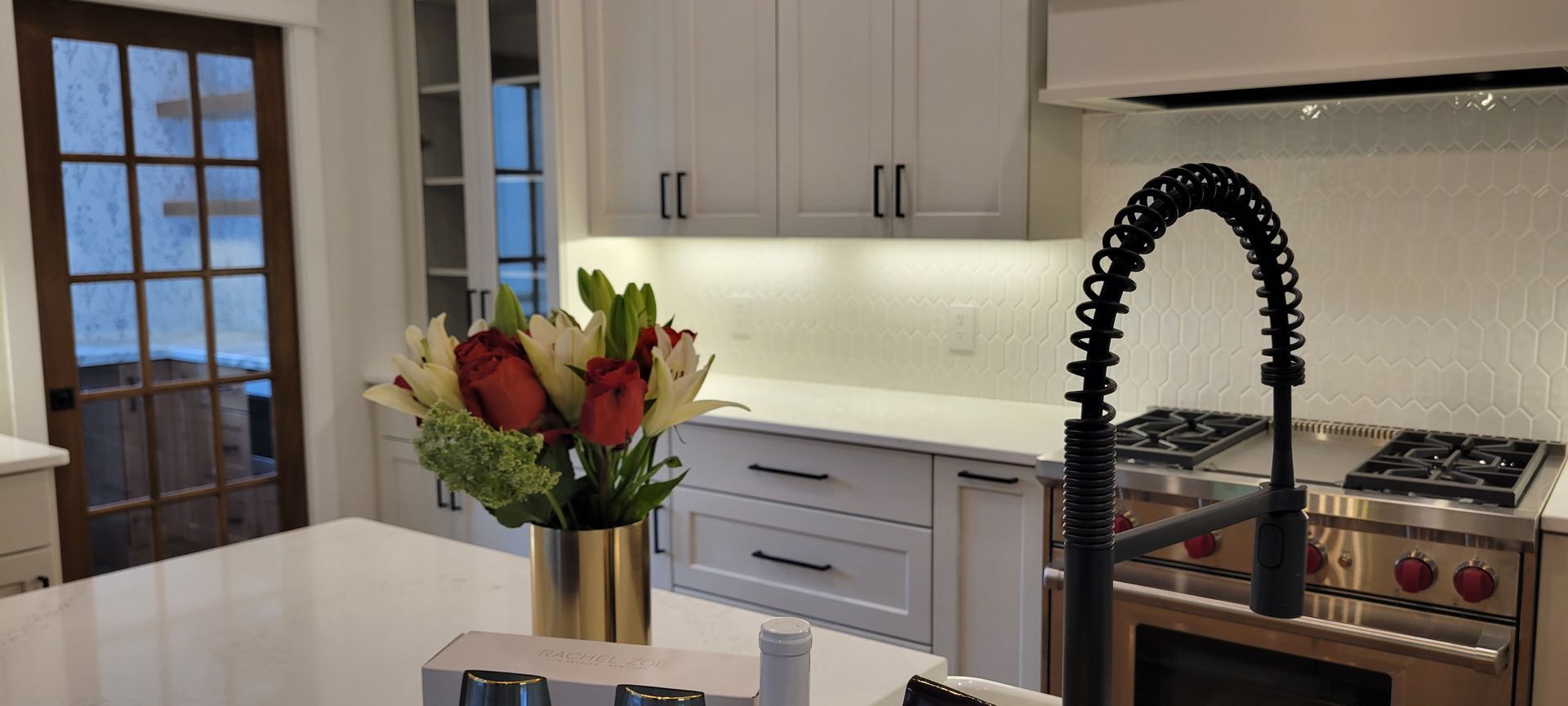 A modern kitchen with white cabinets, a stainless steel stove, and a floral arrangement on a countertop.
