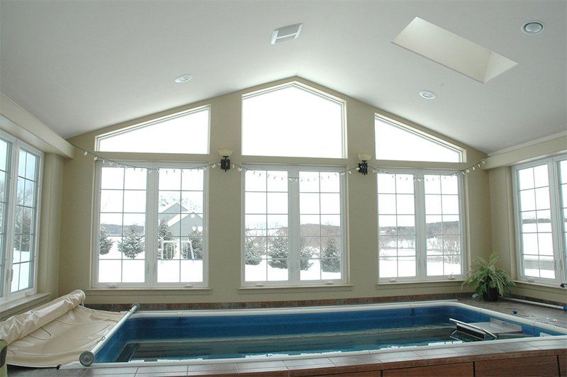 Bright indoor pool room with large windows and a hot tub or spa at the center