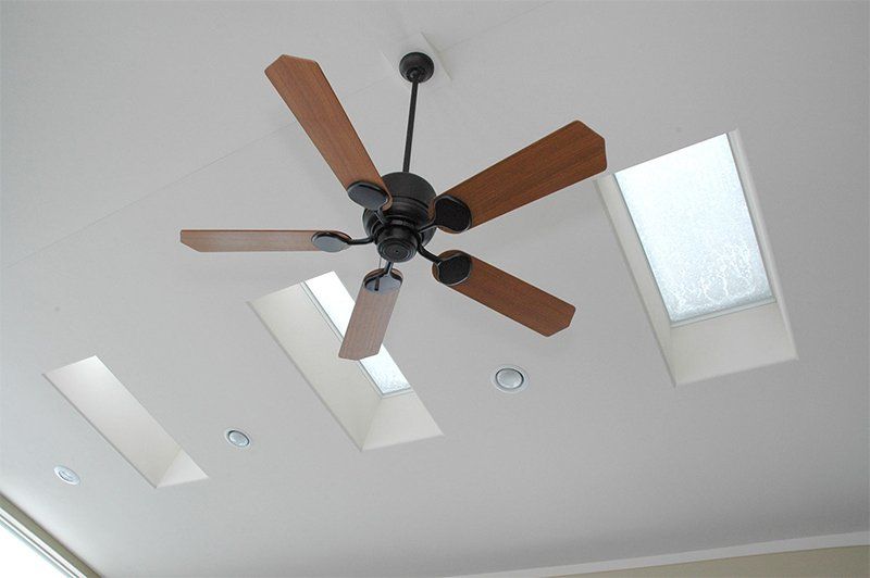 Ceiling fan with wood blades and recessed lights on a white ceiling near skylights