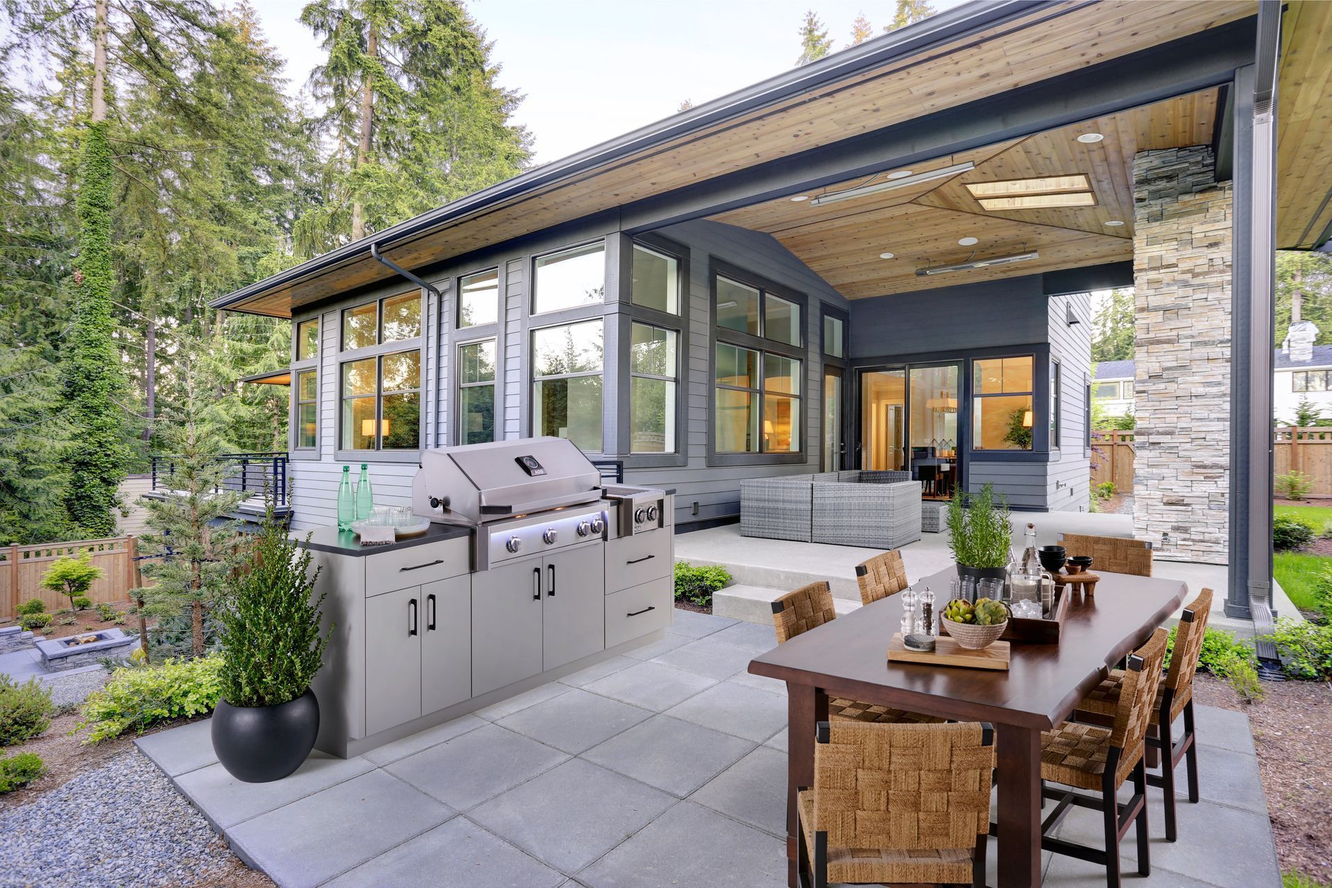 Outdoor patio with stainless steel grill, dining table, and covered seating beside a modern house