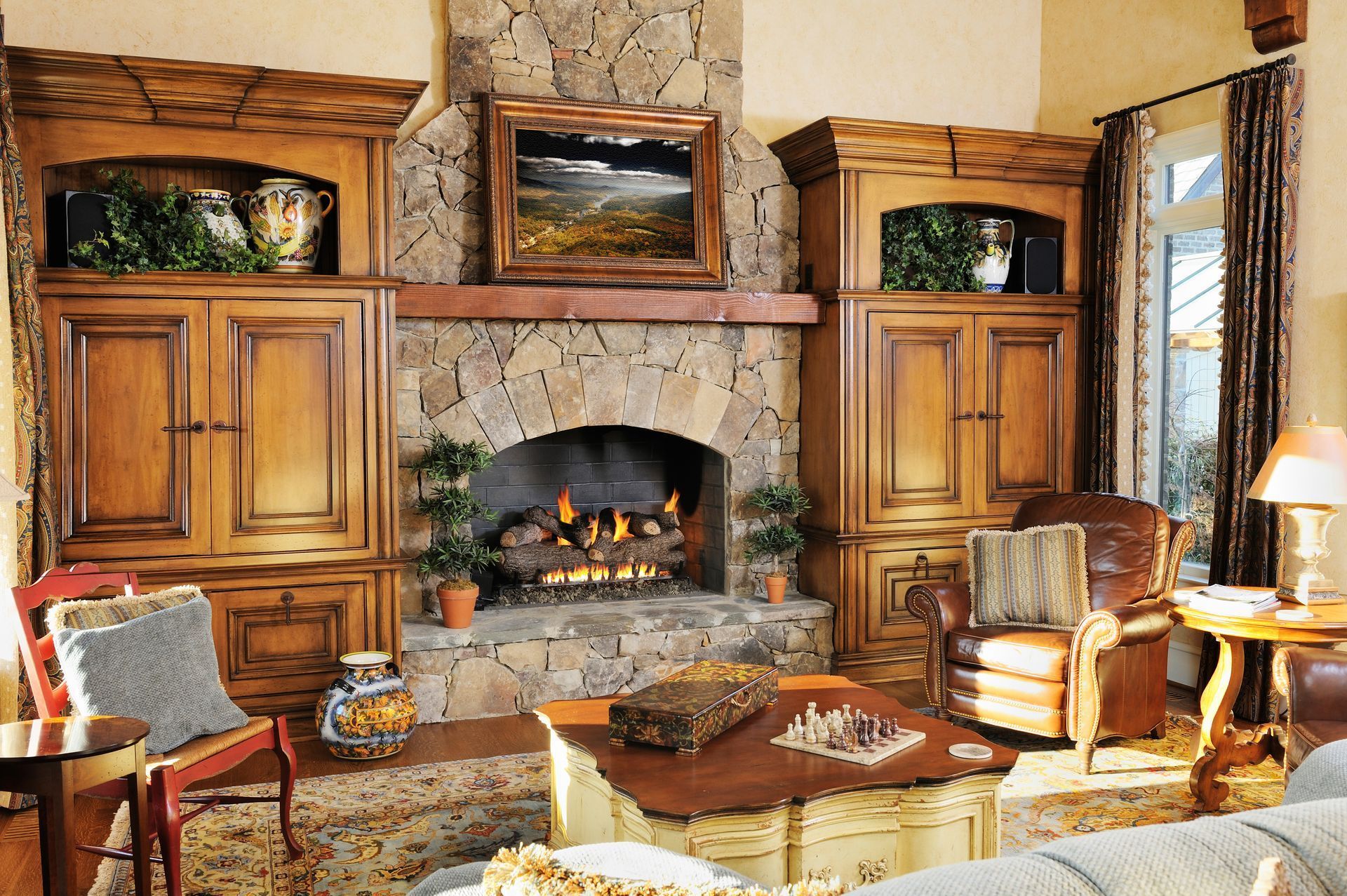 Cozy stone living room with a lit fireplace, and wood cabinets
