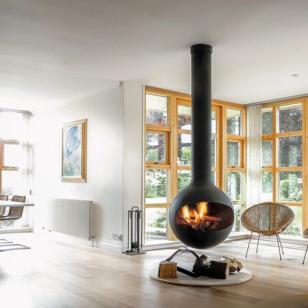 Modern living room with a hanging black fireplace, large windows, and wicker chairs