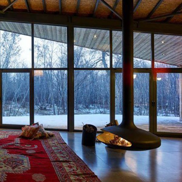 Modern living room with red rug, hanging fireplace, and large windows overlooking snowy trees