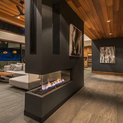 Modern living room with a black double-sided fireplace, wood ceiling, and gray sectional sofa